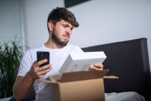Confused man at home opening a messed up delivered package. He looks inhappy with his delivered package.
